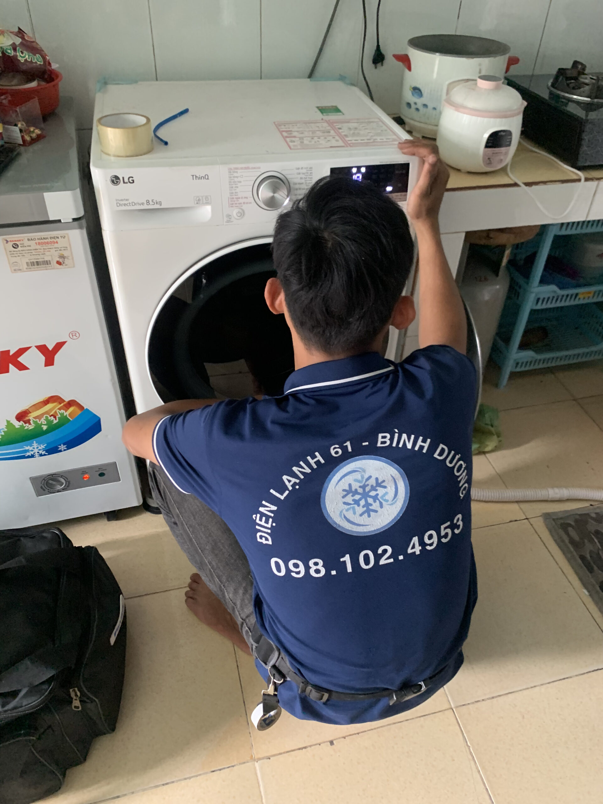 Nhân viên đang vệ sinh khu vực bơm xả nước của máy giặt lồng ngang.