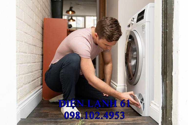 tay đang rút phích cắm máy giặt ra khỏi ổ điện một cách an toàn.