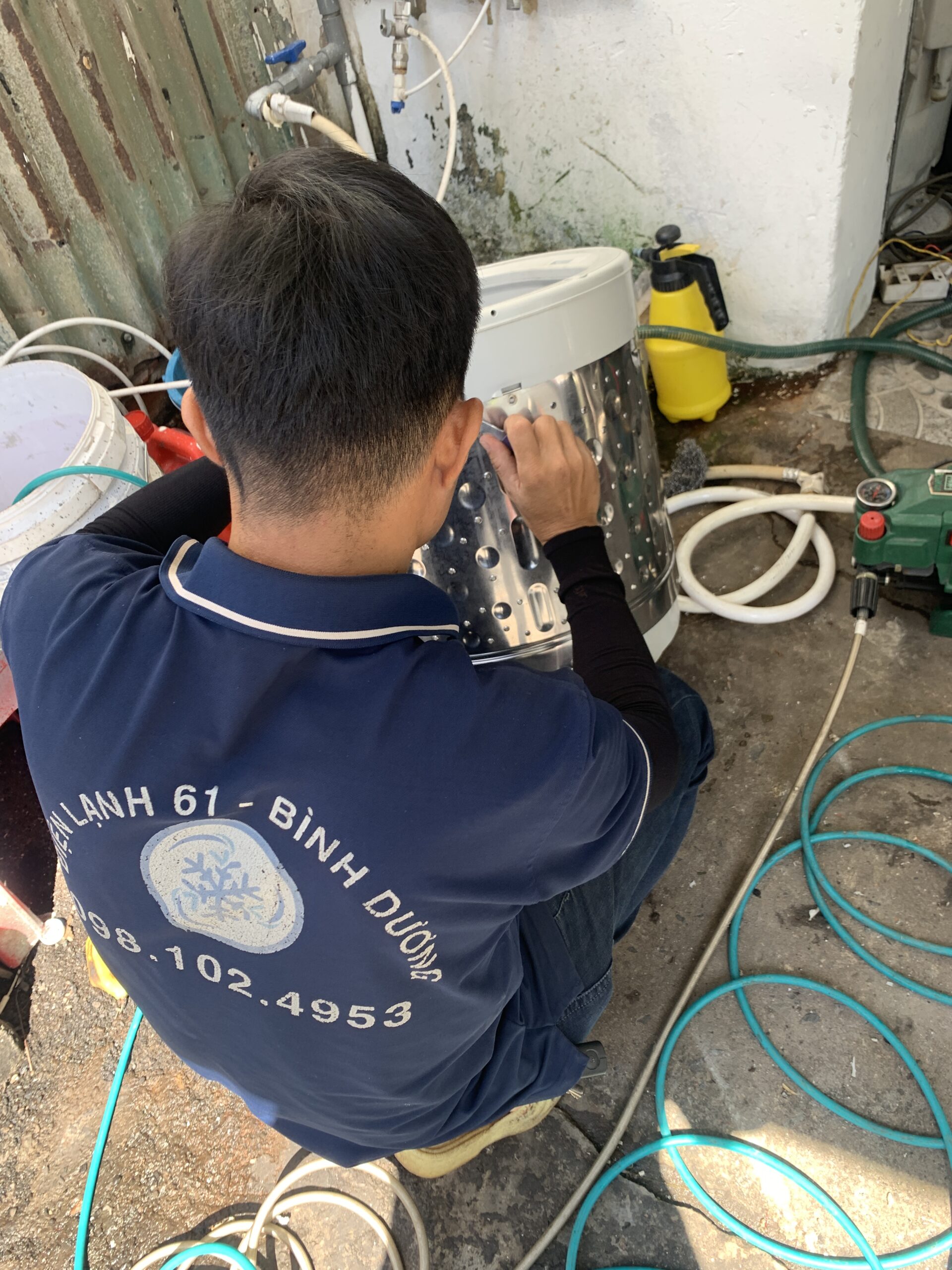 xit-rua-long-giat-bang-may-ap-luc-cao Kỹ thuật viên sử dụng máy bơm áp lực cao xịt rửa sạch sẽ từng ngóc ngách của lồng máy giặt