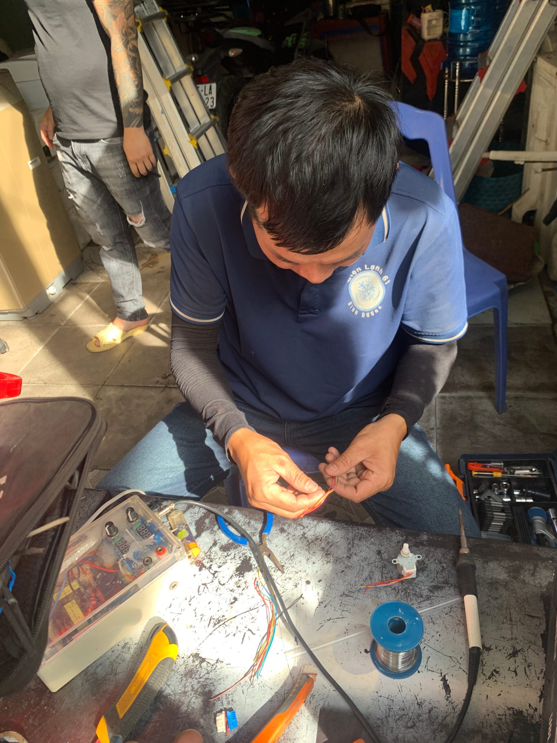 Kỹ thuật viên cầm đồng hồ VOM đo bo mạch máy giặt tại nhà khách hàng