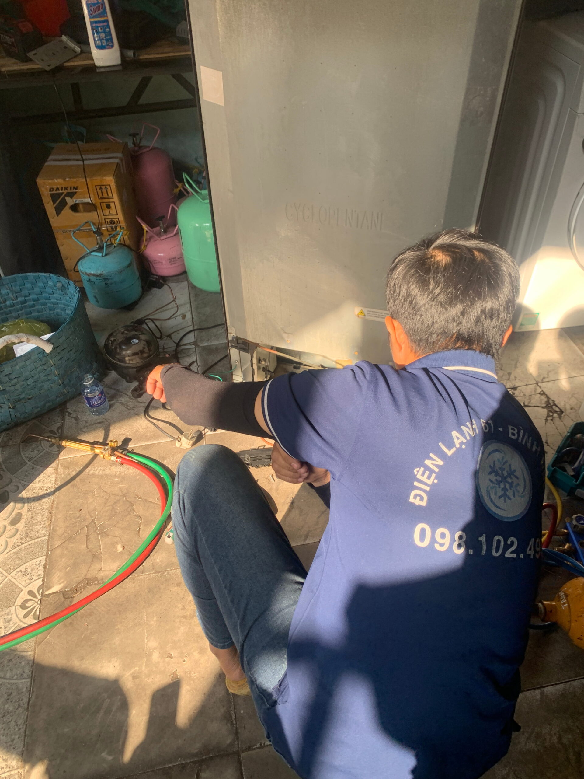 Thợ Điện Lạnh 61 đang dùng đồng hồ đo áp suất và bình gas để nạp cho tủ lạnh tại nhà.