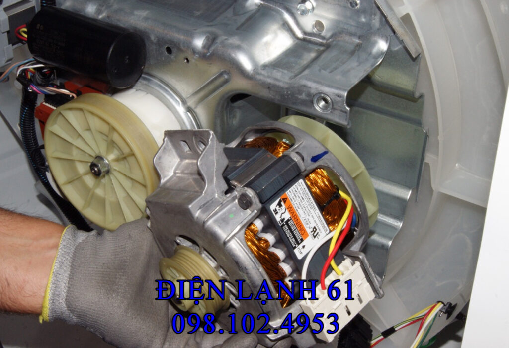 Thợ Điện Lạnh 61 đang kiểm tra phần động cơ phía sau một chiếc máy giặt cửa ngang.