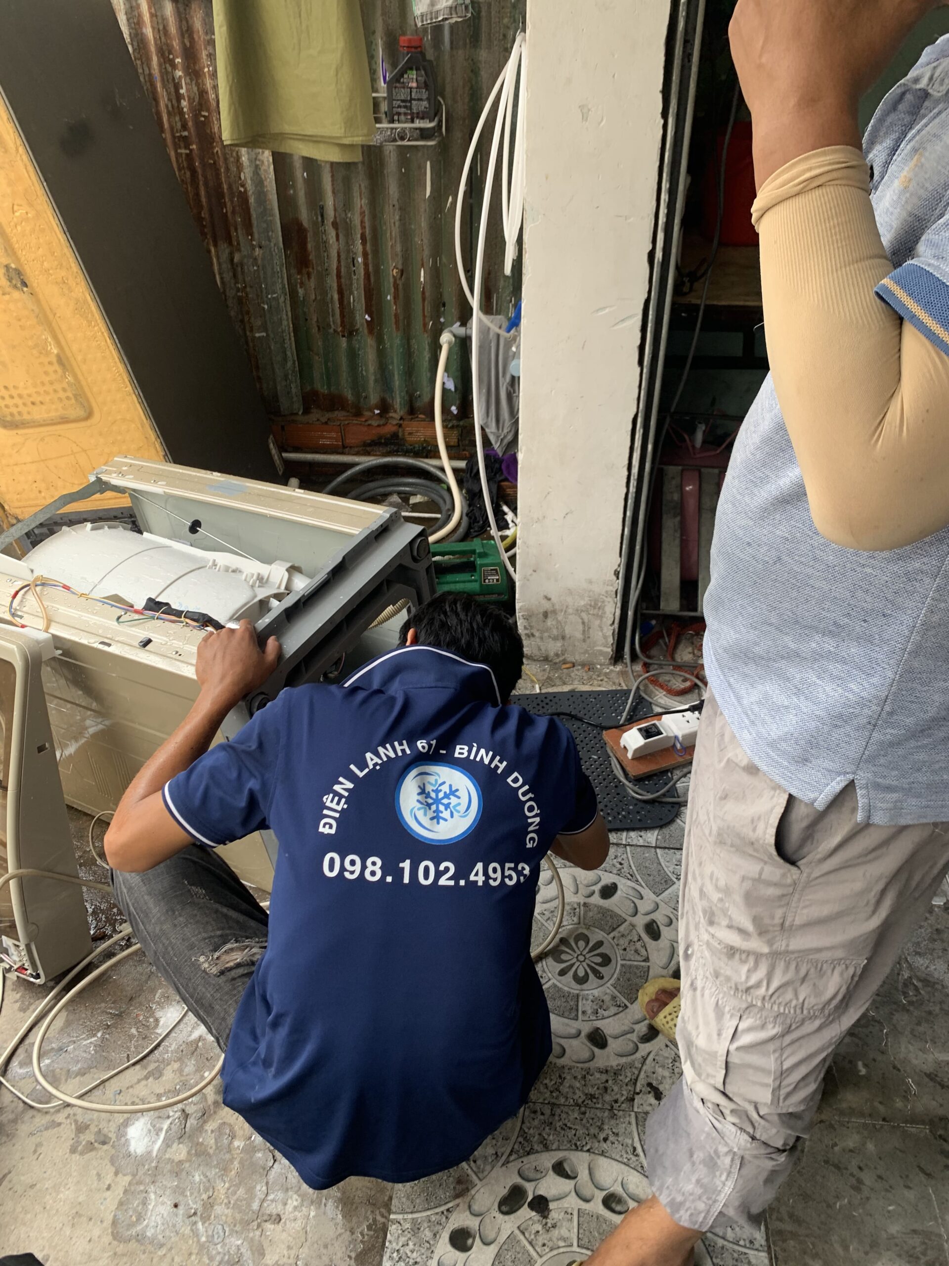 Thợ Điện Lạnh 61 đang kiểm tra phần dưới đáy máy giặt, có nước chảy ra khay.