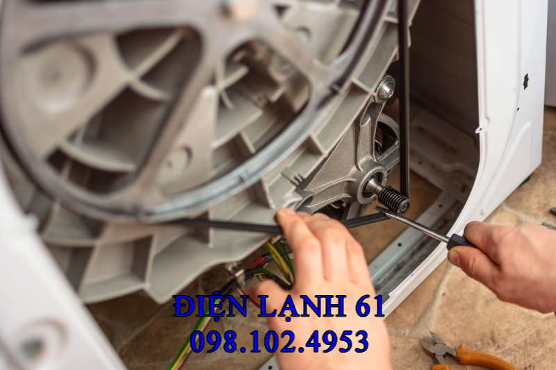 Thợ Điện Lạnh 61 đang kiểm tra phần gầm máy giặt, tay chạm vào dây curoa.