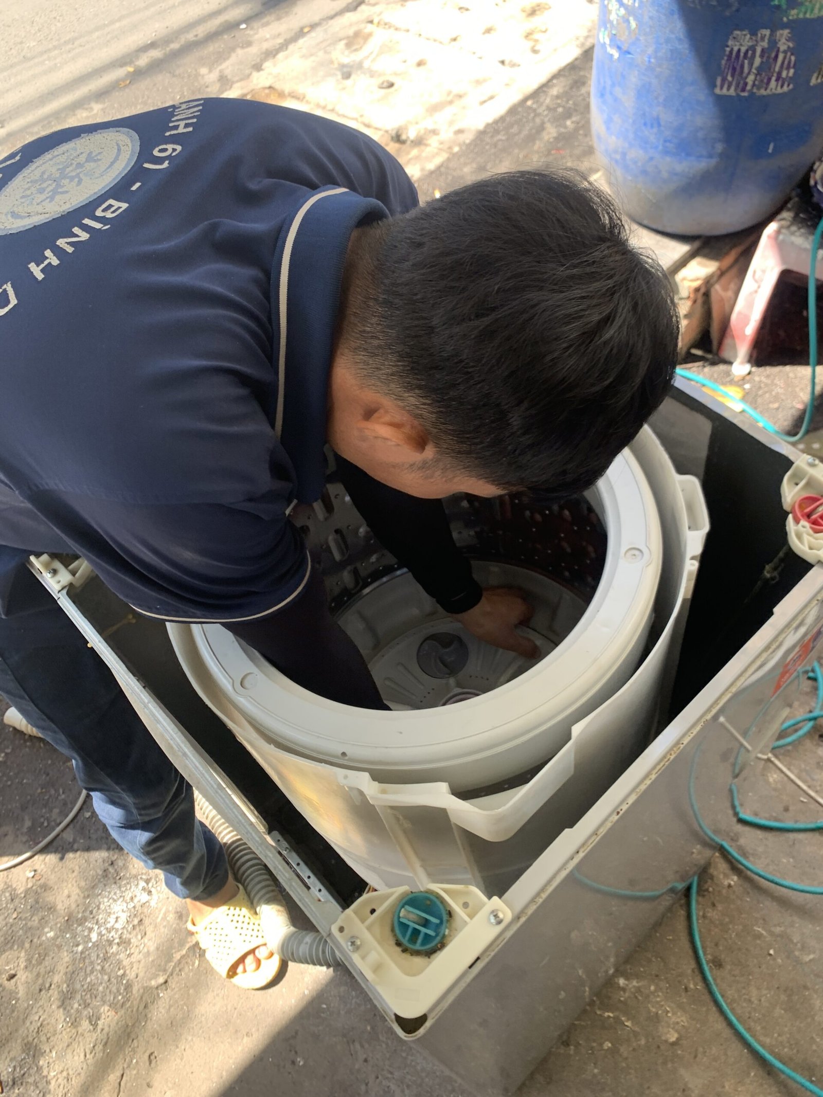 Kỹ thuật viên đang nhấc và móc thanh ty treo mới vào lồng giặt.